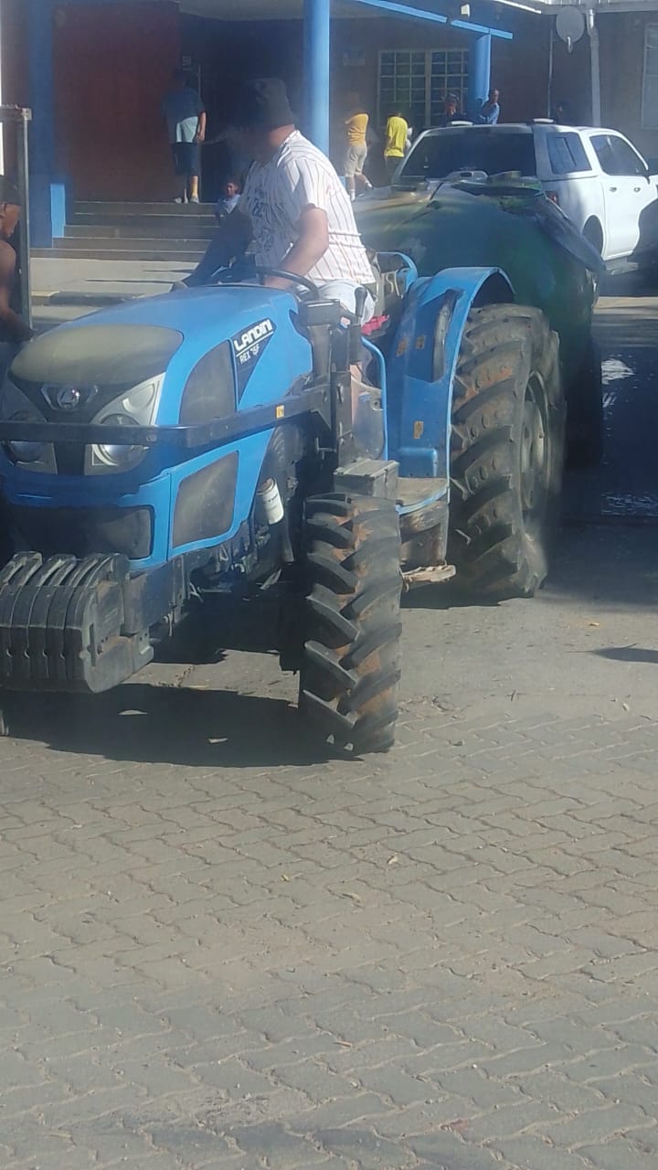 A blue Landini tractor driving across the school's paved forecourt